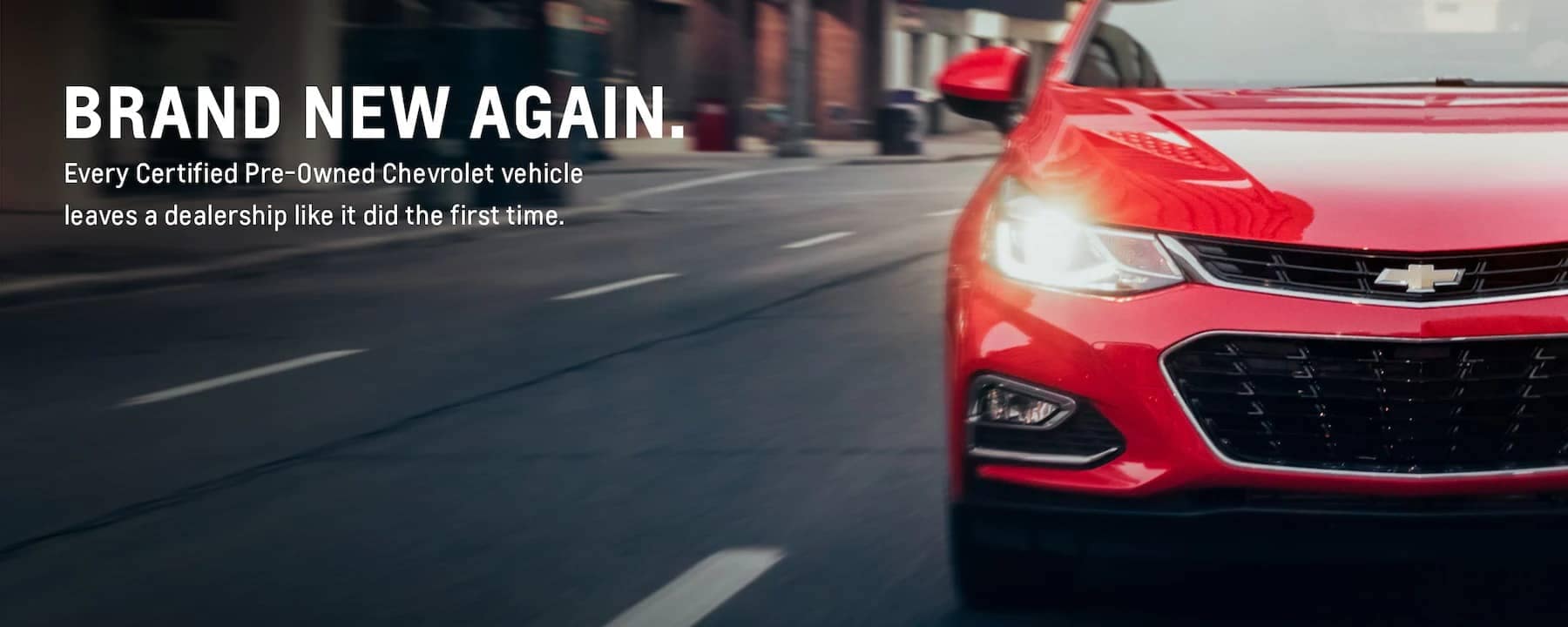 A dynamic shot of a bright red Chevrolet vehicle driving on a city street, showcasing its sleek design and modern features, emphasizing the concept of certified pre-owned vehicles looking brand new.