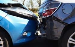 Close-up of a blue car and a gray car involved in a rear-end collision, highlighting damage to both vehicles' bumpers.