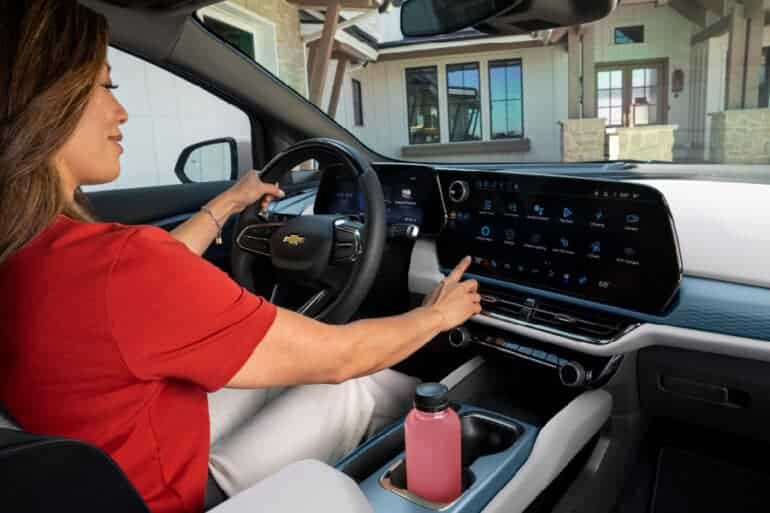 Interior view of a Chevrolet vehicle showcasing a woman interacting with the touchscreen display while driving, with a modern dashboard and a beverage in the center console.