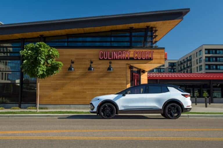 White electric SUV parked in front of a modern building named Culinary Court, featuring a wooden facade and large windows, with additional modern residential structures in the background under a clear blue sky.