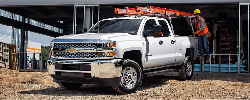 White heavy-duty truck parked at a job site with a ladder on the roof and workers nearby.