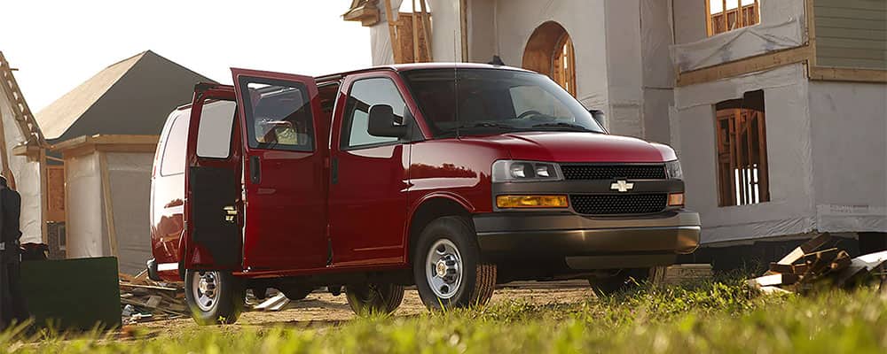 Red commercial van parked outside a large building under construction with its doors open.