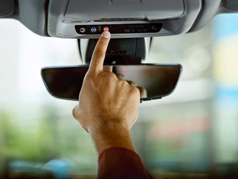 Person pressing the OnStar button on a car’s rearview mirror, activating safety or assistance services.