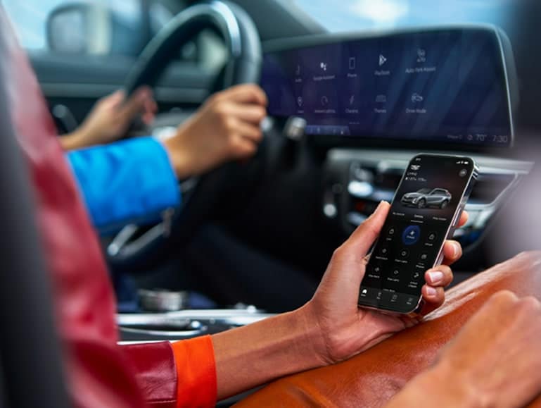Close-up of a person using the OnStar mobile app inside a vehicle, with another person driving