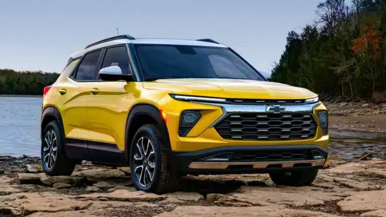 Modern yellow Chevrolet SUV parked on rocky shoreline with forest background, showcasing its sleek design and off-road capabilities.